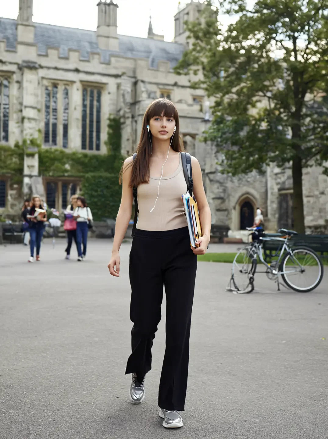 A young woman in 98degreenorth Black Women’s Fleece Flared Sweatpants walks campus with books, headphones, bikes nearby.