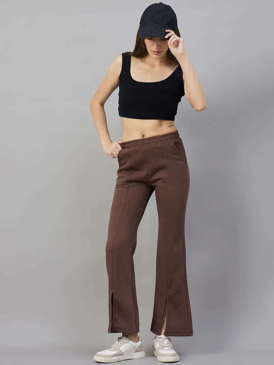 Woman wears 98degreenorth Cocoa Brown Fleece Flared Sweatpants, black crop top, white sneakers, and black cap.