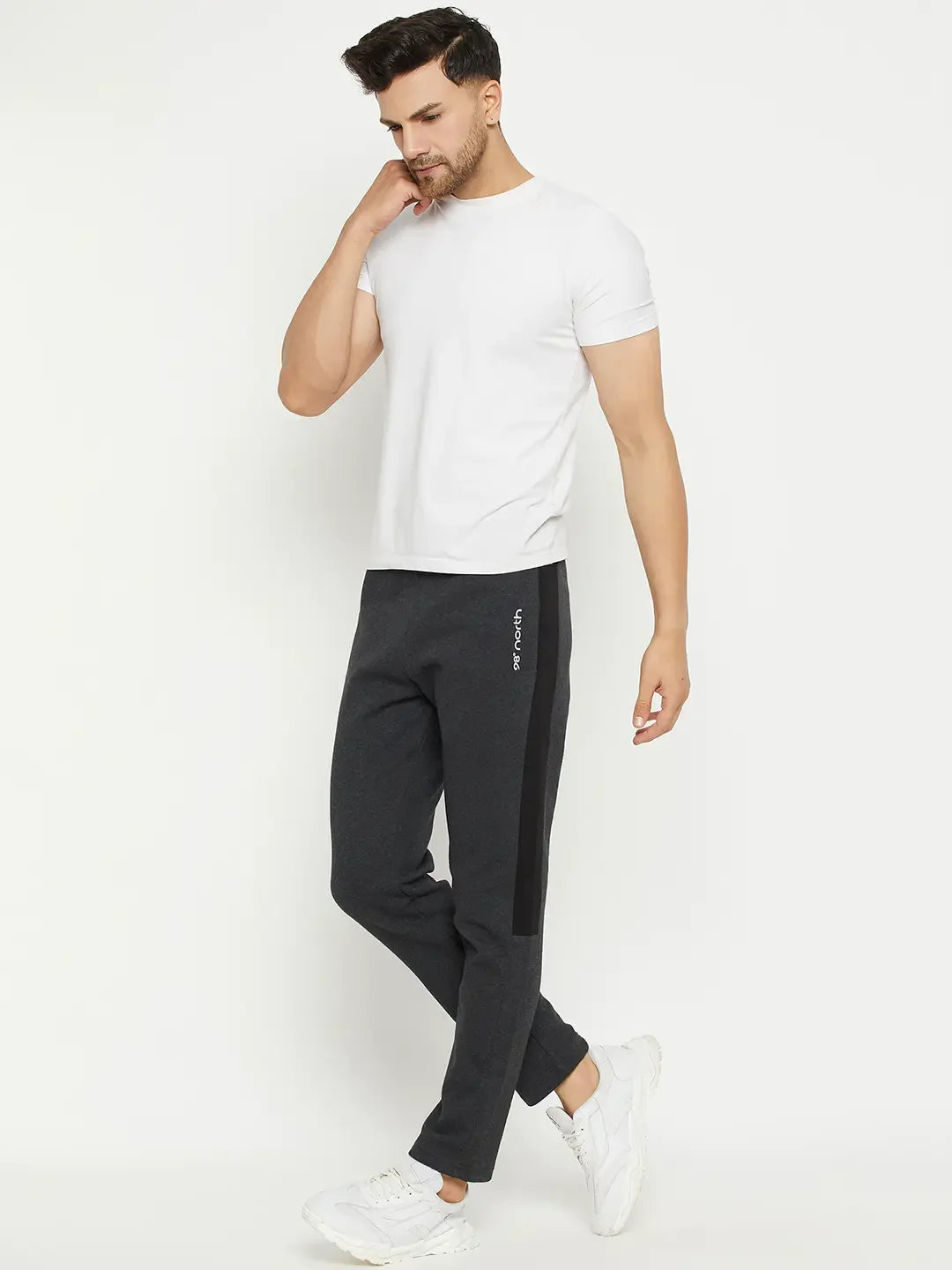 Man in a white tee, 98degreenorth Anthra Fleece Trackpants, and white sneakers stands against a white background.