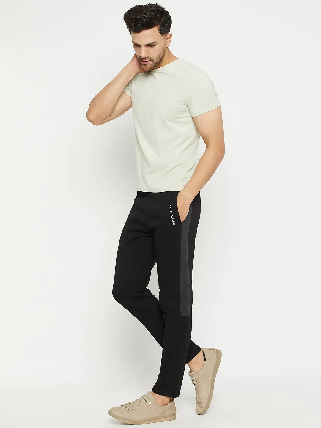 Man in 98degreenorth beige tee, Men’s Black Fleece Trackpants with Side Design, and beige sneakers on white background.