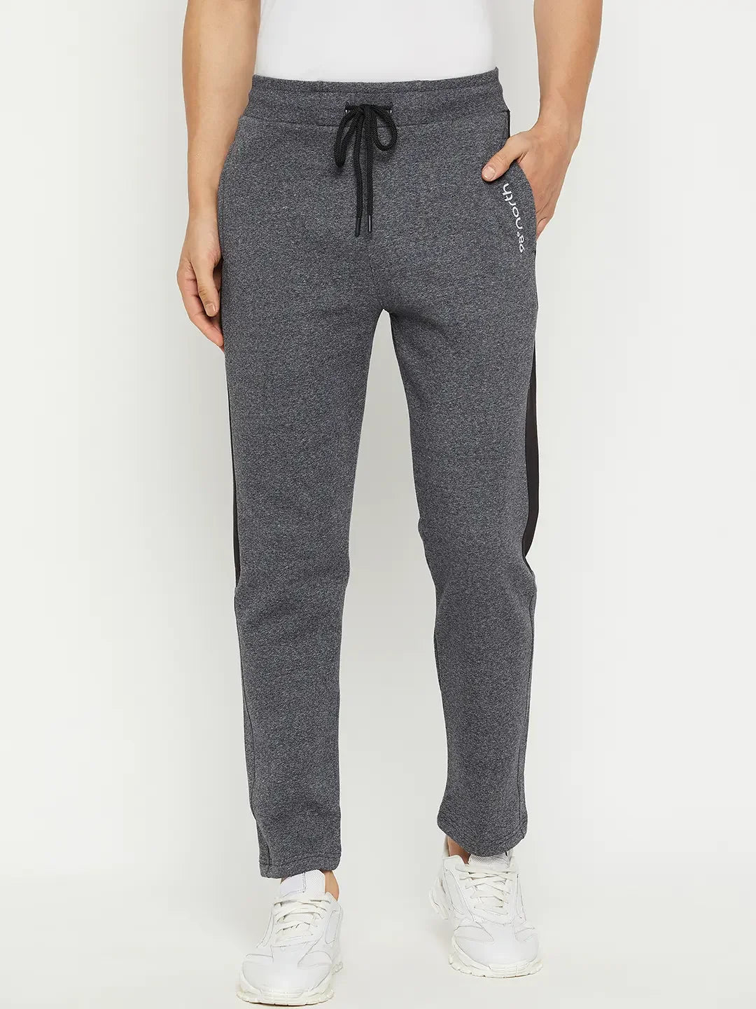 Man in 98degreenorth Black Jaspe fleece trackpants with side panel, white shirt, and sneakers against a plain background.