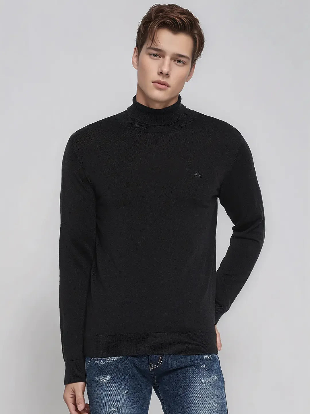 Young man wears 98degreenorth’s Men’s Black Merino Wool Turtle Neck Sweater with blue jeans against a light gray background.