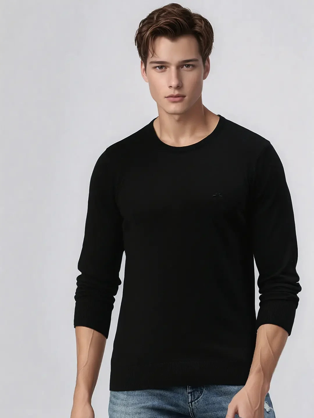 A man wears a 98degreenorth men's black merino wool luxury knit pullover with blue jeans against a light background.