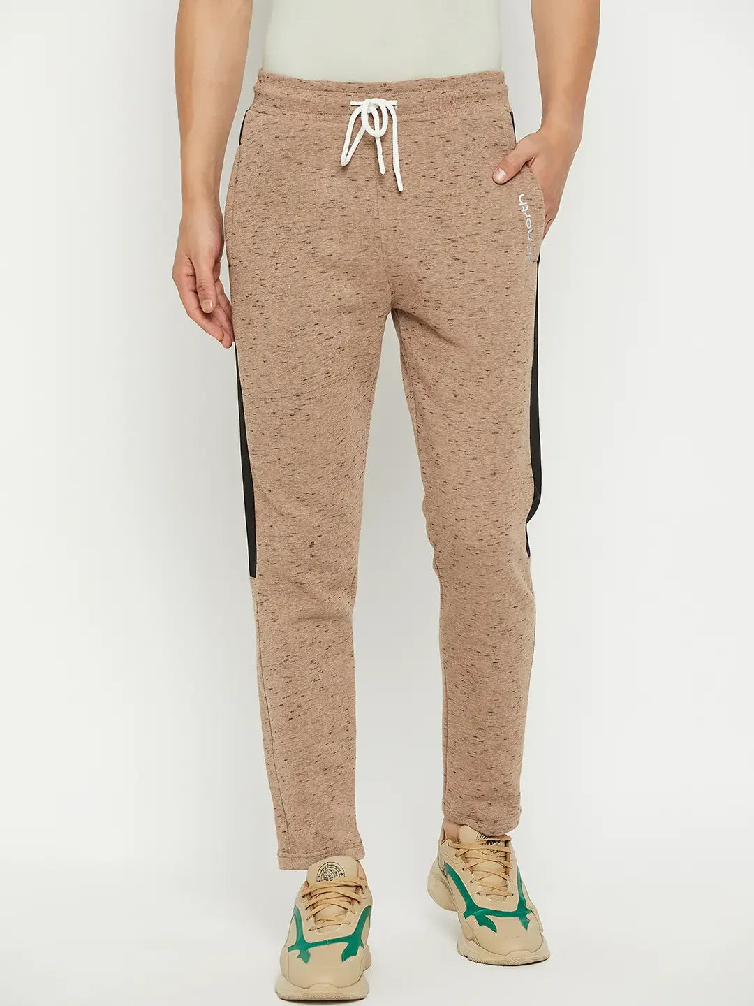Wearing 98degreenorth Men’s Camel Fleece Trackpants with contrast stripe and beige sneakers with green accents.
