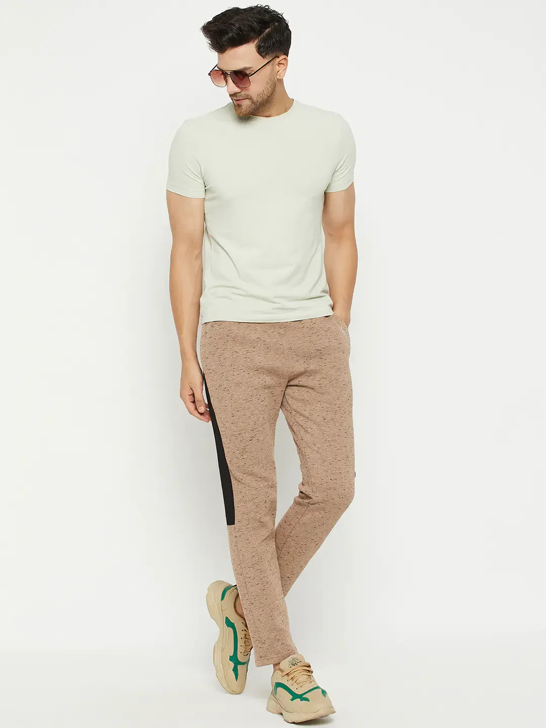 Man in sunglasses, light green tee, 98degreenorth camel fleece trackpants with side stripe, tan sneakers on white backdrop.