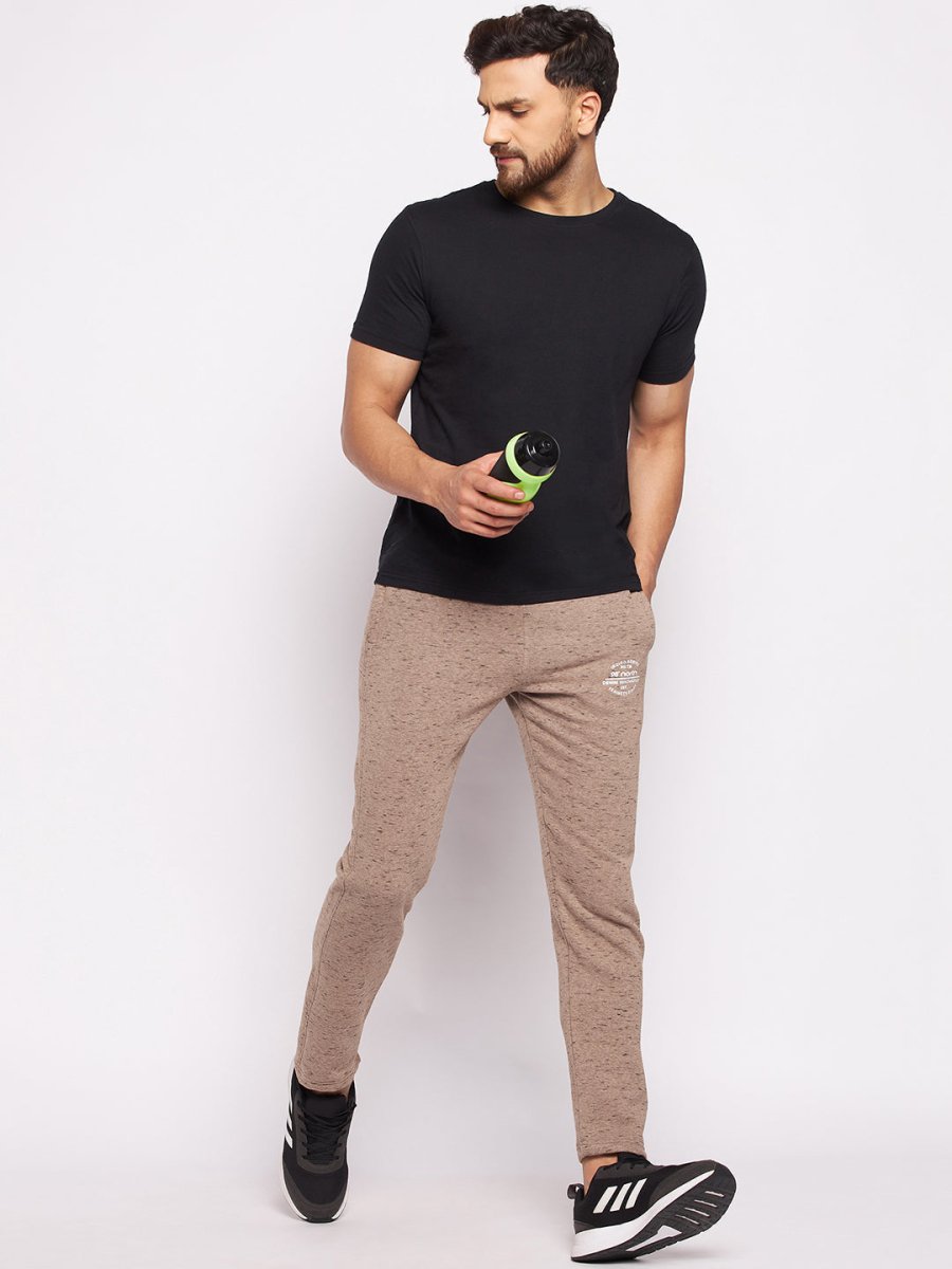 A man in a black t-shirt and 98degreenorth Men’s Camel Melange Fleece Trackpants holds a green water bottle, looking left.