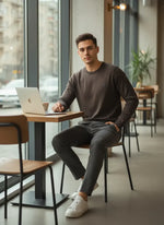 A man in a 98degreenorth Men’s Charcoal Merino Wool Sweater works at a cafe table with city views behind him.