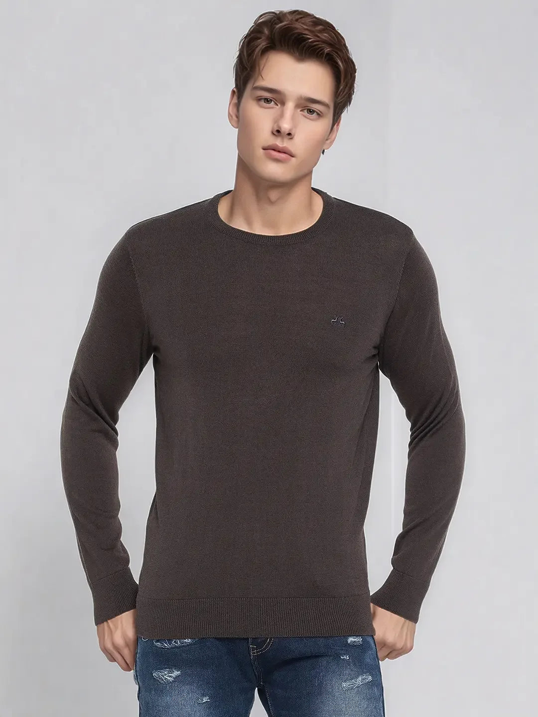 A man wears the 98degreenorth Men’s Charcoal Merino Wool Sweater, pairing it with blue jeans against a gray background.