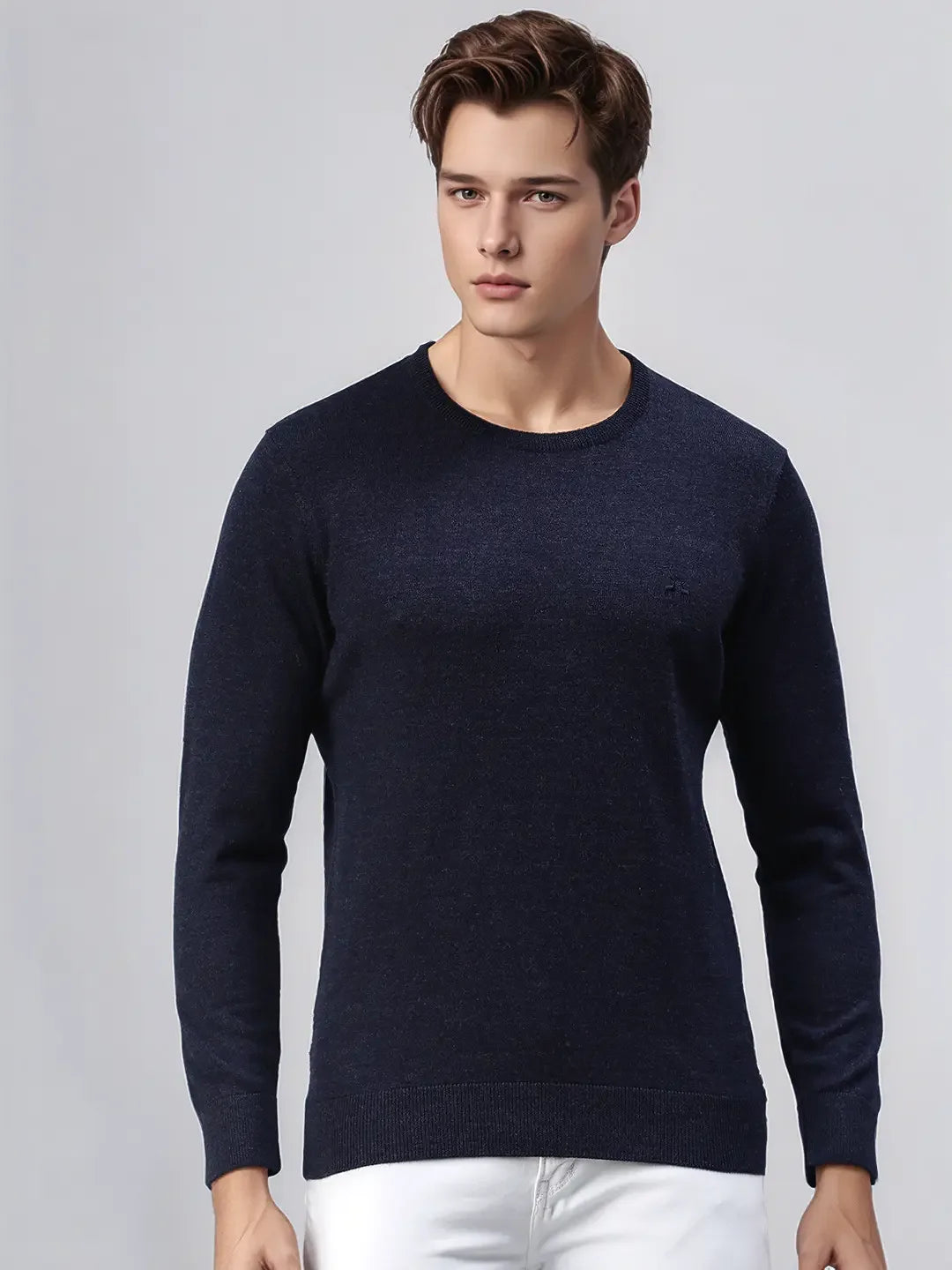 A man wears a 98degreenorth Dark Denim Merino Wool Round Neck Sweater with white pants against a light gray background.