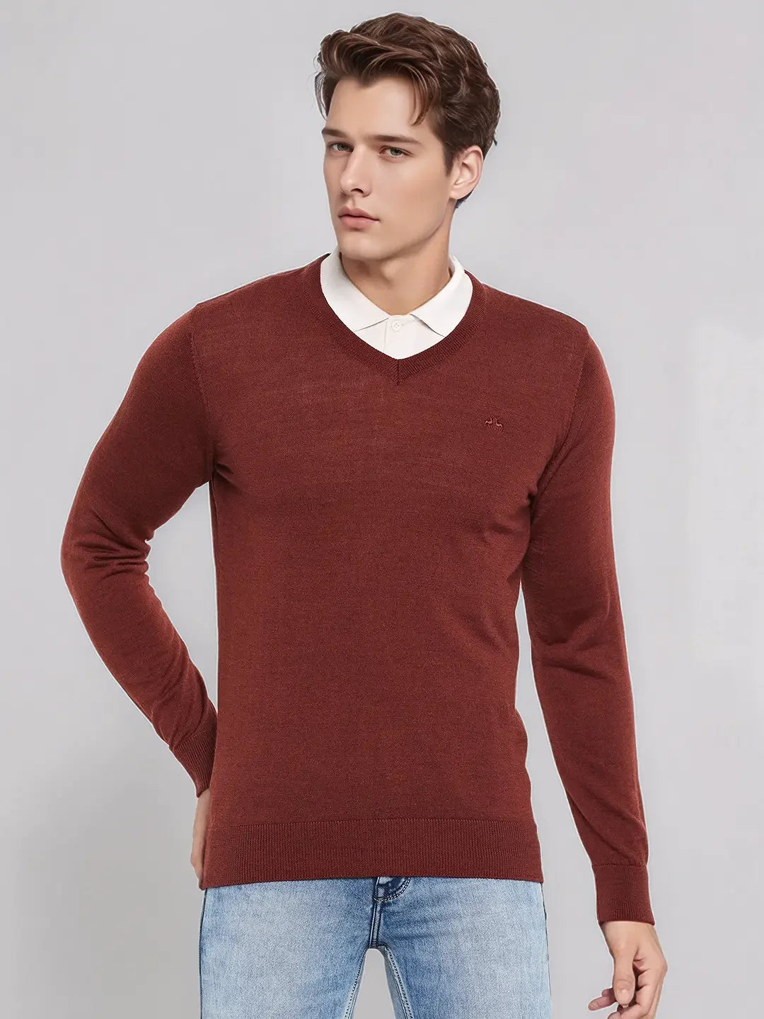 A man wears the 98degreenorth Men’s Dark Maroon Merino Wool V-Neck Sweater over a white shirt and light blue jeans.