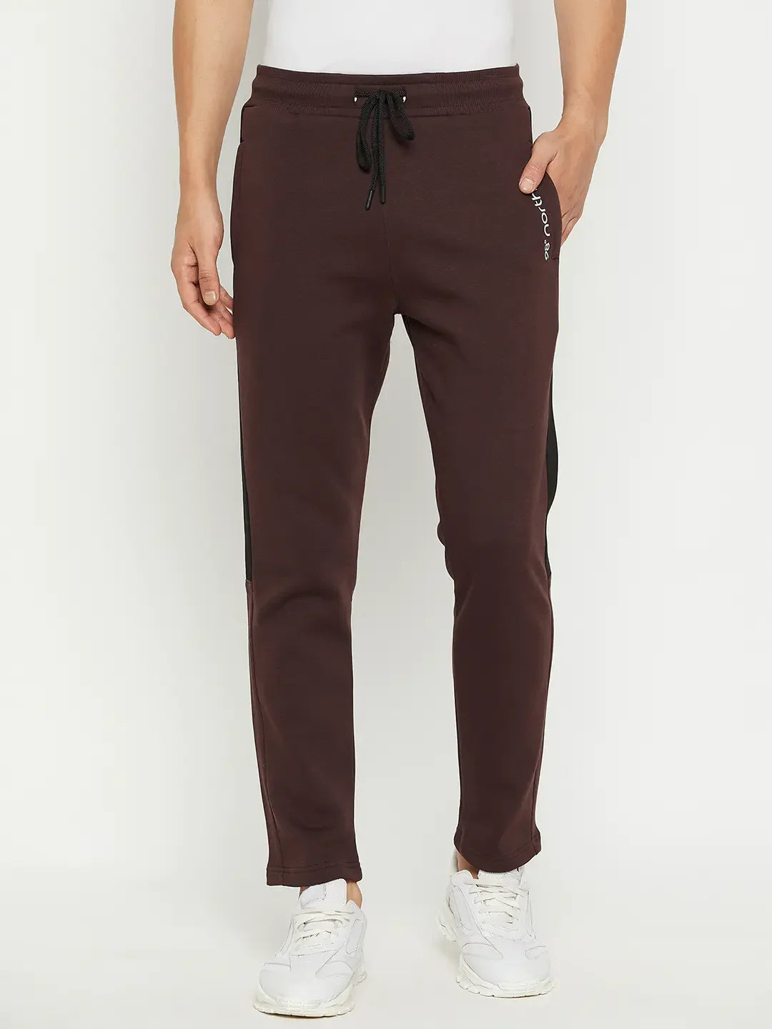A man in 98degreenorth Men’s Dark Wine Fleece Trackpants with side panels and white sneakers stands against a plain backdrop.