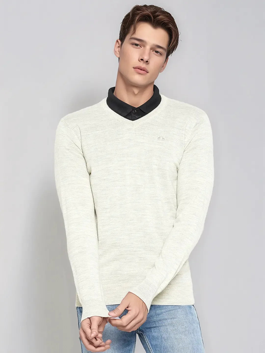 Young man wears 98degreenorth Men’s Ecru Merino Wool V-Neck Sweater over black shirt, against gray backdrop.