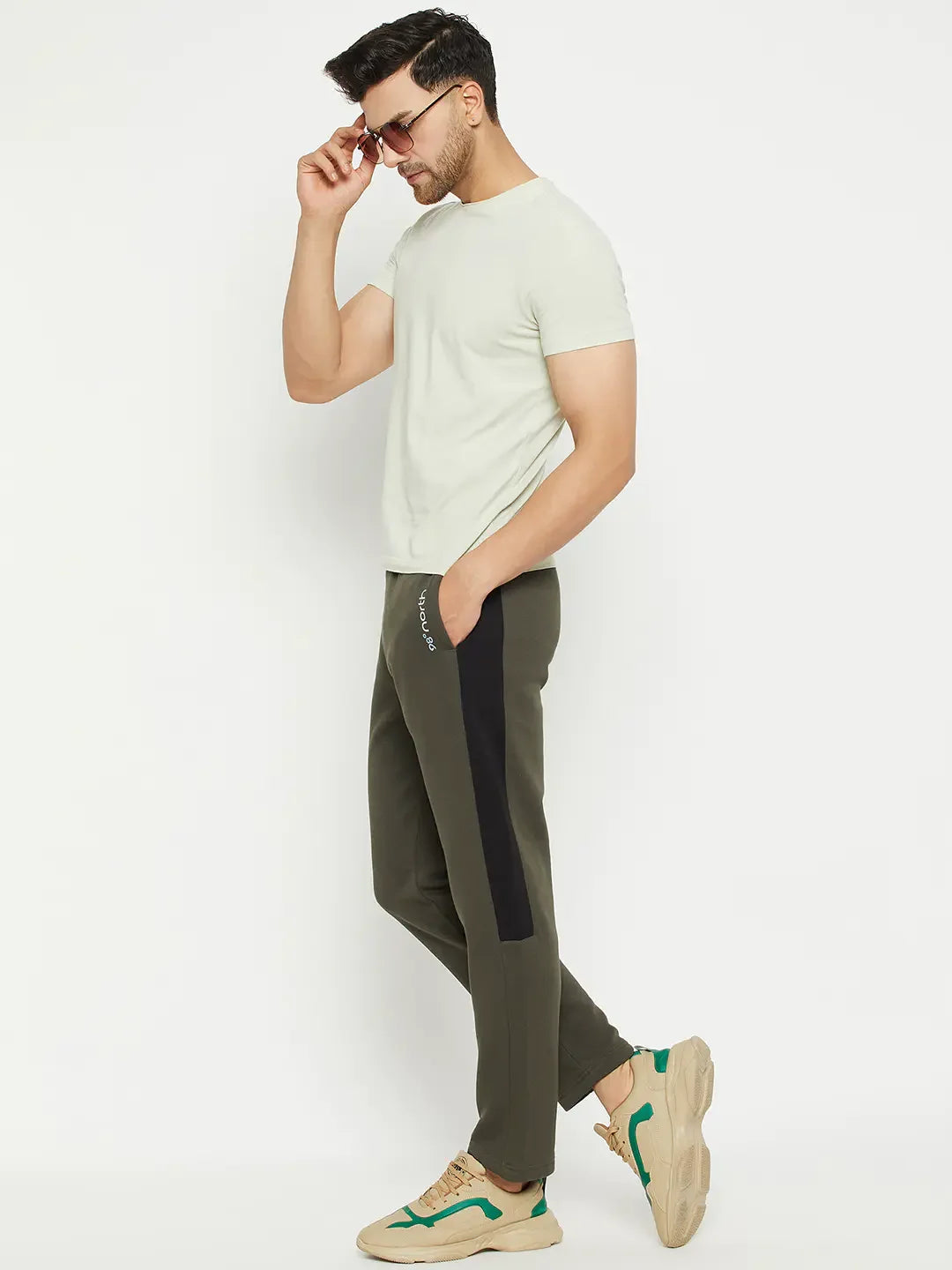 Man in sunglasses and light tee wears 98degreenorth olive fleece trackpants with side panel, plus beige sneakers, sideways.