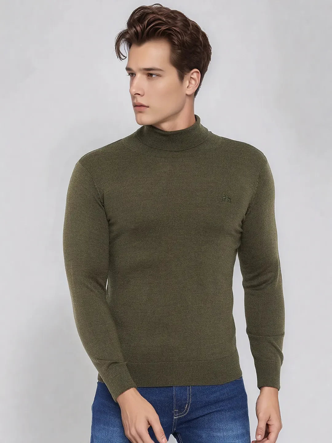 A man in a 98degreenorth olive merino wool turtle neck sweater and blue jeans stands against a light gray background.