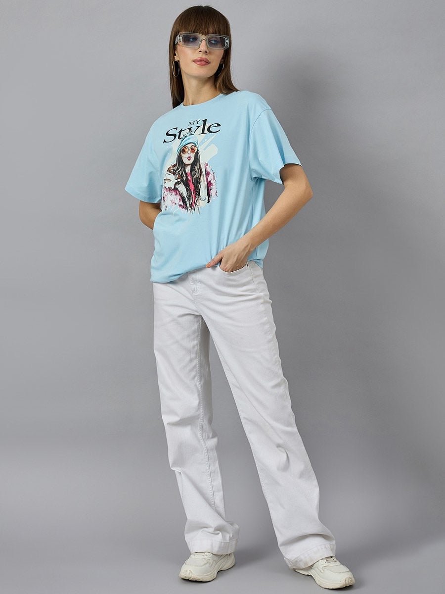 Woman in 98degreenorth Soft Cotton Typography Printed Tee with drop shoulder sleeves poses in white pants and sneakers.