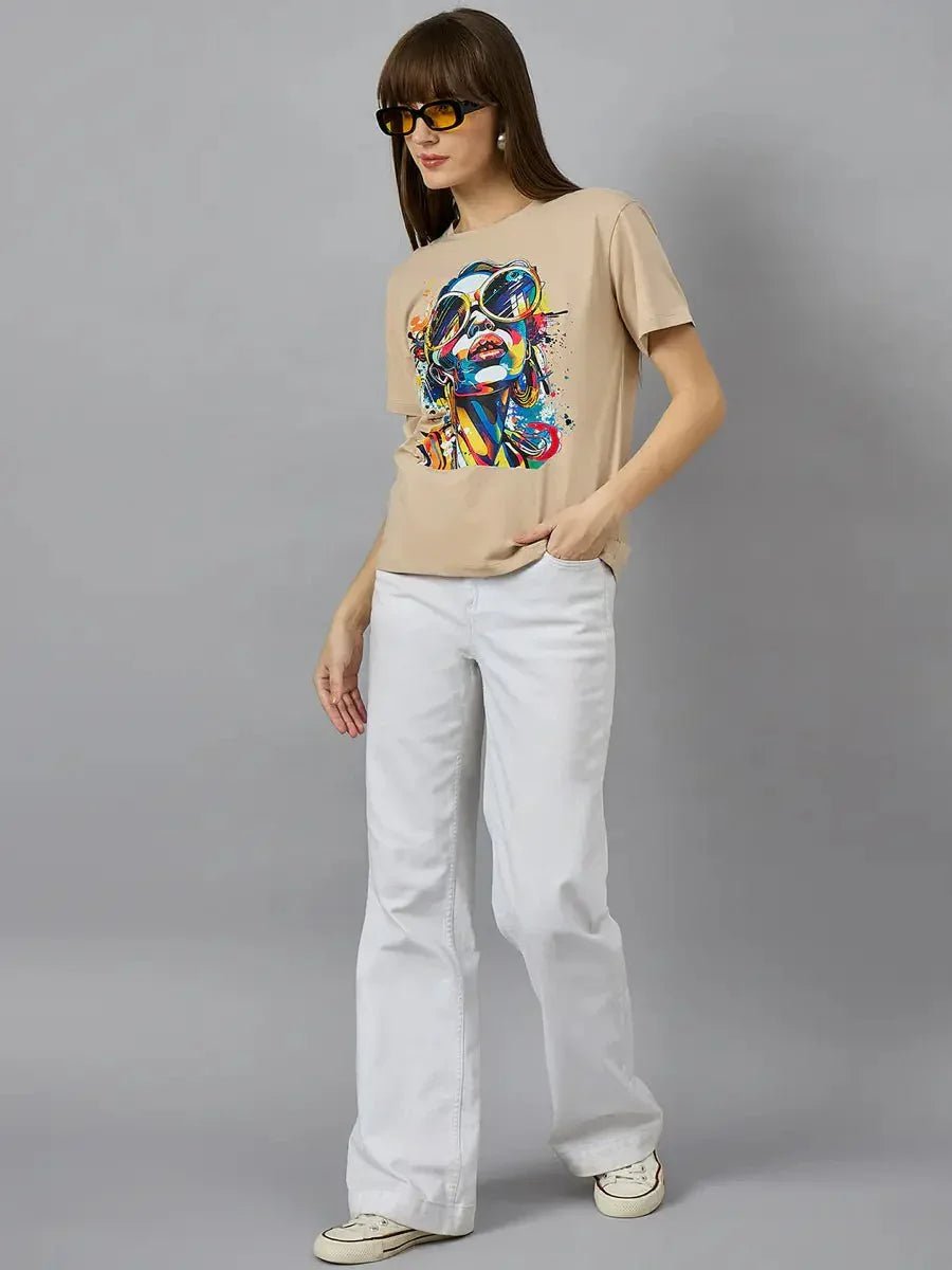 Woman in sunglasses wears 98degreenorth Typography Print Women’s Cotton T-shirt and white flared pants against gray background.