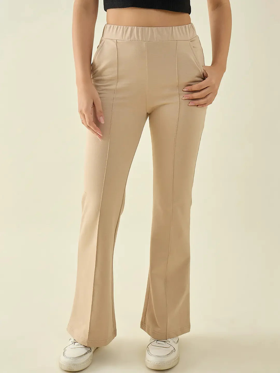 Model in 98degreenorth Women’s Beige Flared Bootcut Cotton Stretchable Trousers, paired with a black top and white sneakers.