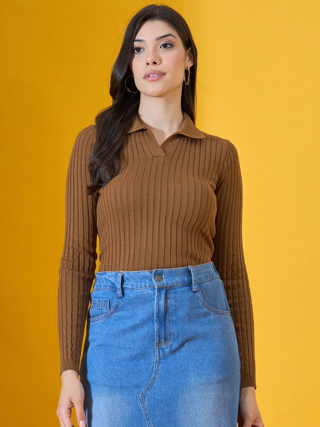 Woman in a 98degreenorth brown ribbed collar neck slim fit sweater and denim skirt against a yellow background.