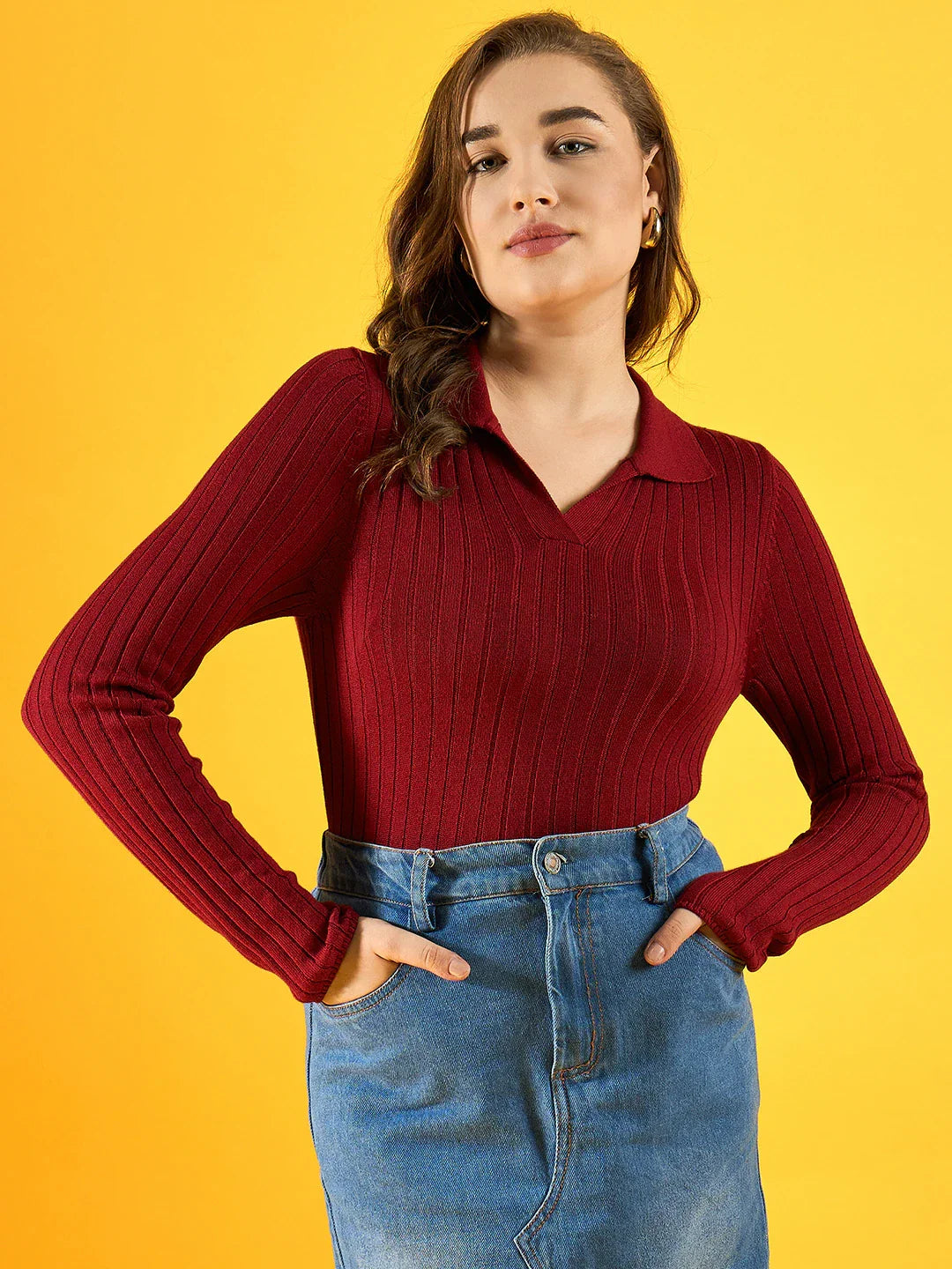 Woman wears 98degreenorth’s maroon ribbed collar neck slim fit sweater with a blue denim skirt, posing against yellow.