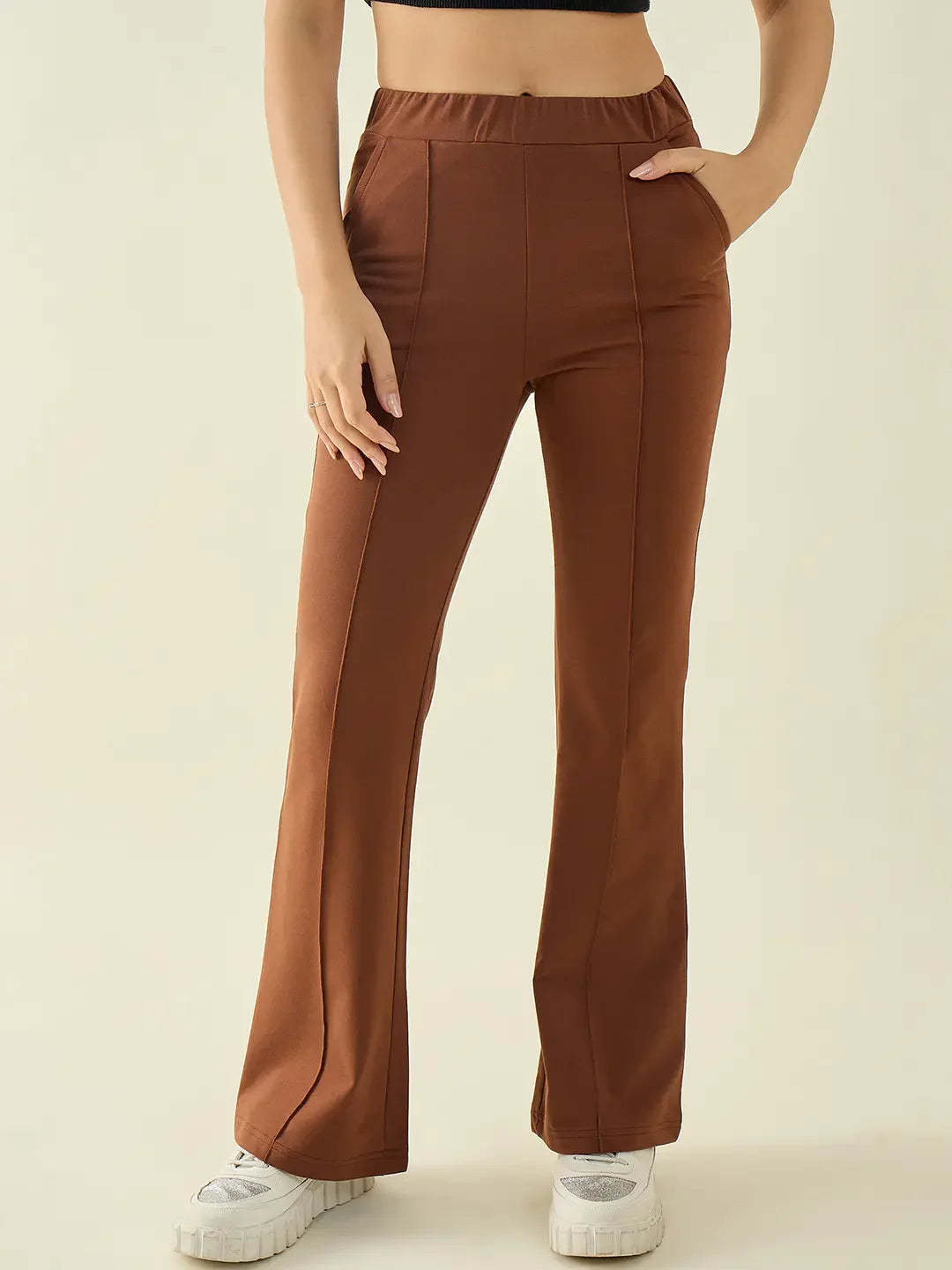 Person in 98degreenorth rust flared bootcut trousers, black crop top, and white sneakers stands against a plain background.