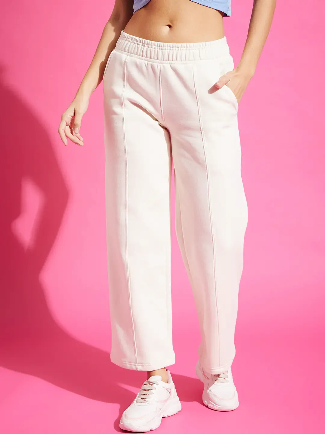 A woman in 98degreenorth Butter Straight Fit Fleece Sweatpants stands against a bright pink background.