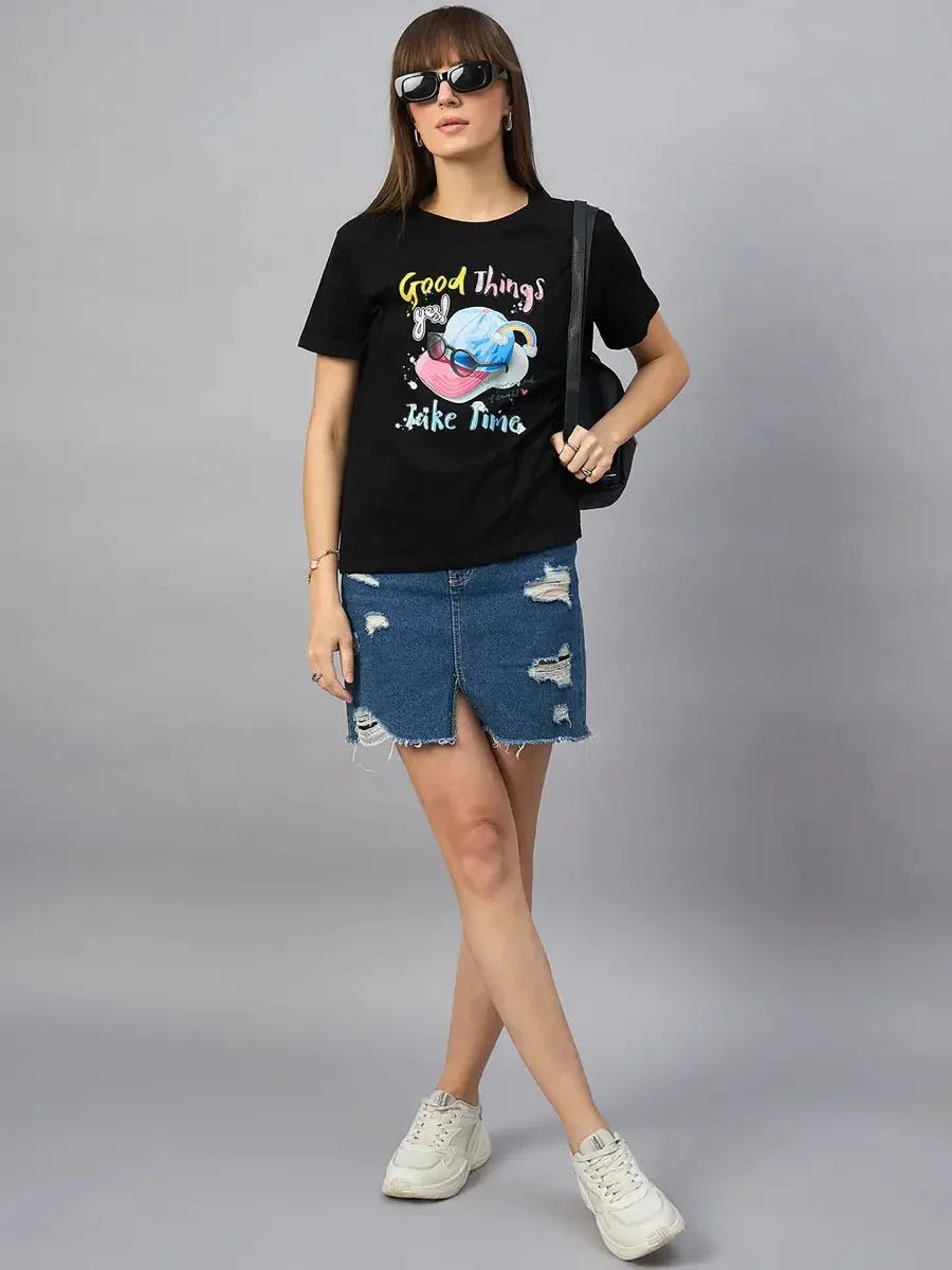 Woman in 98degreenorth Women’s Typography Printed Cotton Tee, denim skirt, white sneakers, on grey background.