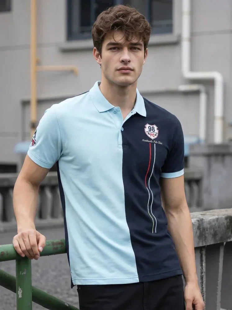 Man wearing a mustard brown short-sleeve polo shirt and light blue jeans, standing against a plain white background, looking to his left with one hand by his side.