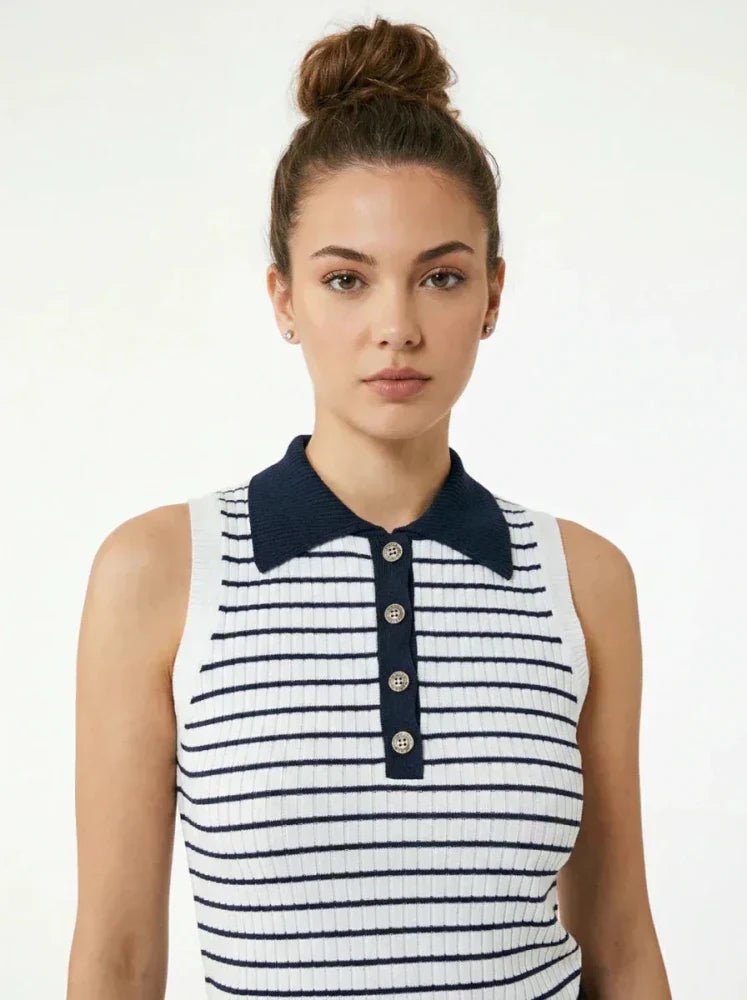 A woman with brown hair in a bun wears a sleeveless white top with navy blue horizontal stripes, a navy blue collar, and a button placket. She stands against a plain light background.
