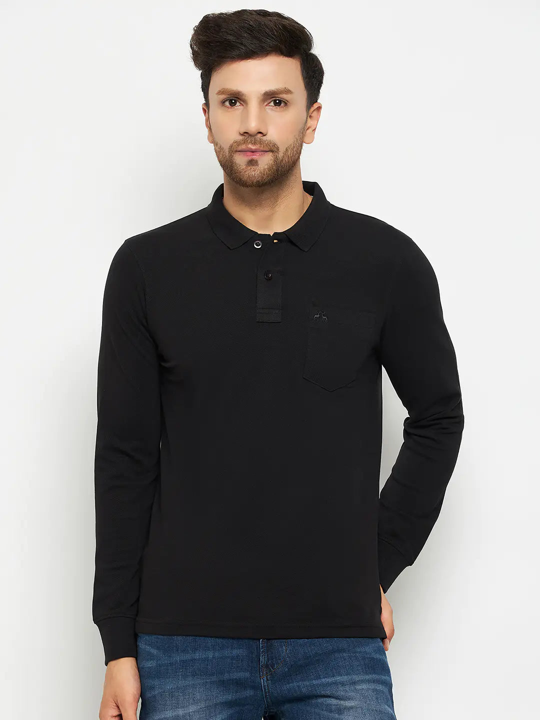 A man wearing a black long-sleeve polo shirt with a chest pocket and blue jeans stands against a plain white background, looking straight ahead.