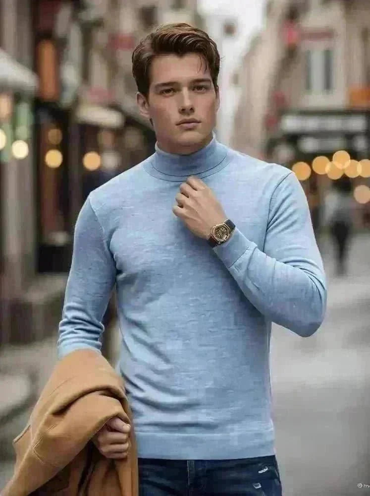 A man walks on a cobblestone street in winter, wearing a burgundy turtleneck, blue jeans, and brown boots, holding a tan coat. Snow is on the ground, and outdoor lamps and buildings line the street.