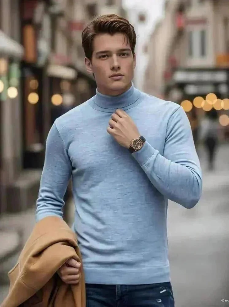 A man walks on a cobblestone street in winter, wearing a burgundy turtleneck, blue jeans, and brown boots, holding a tan coat. Snow is on the ground, and outdoor lamps and buildings line the street.