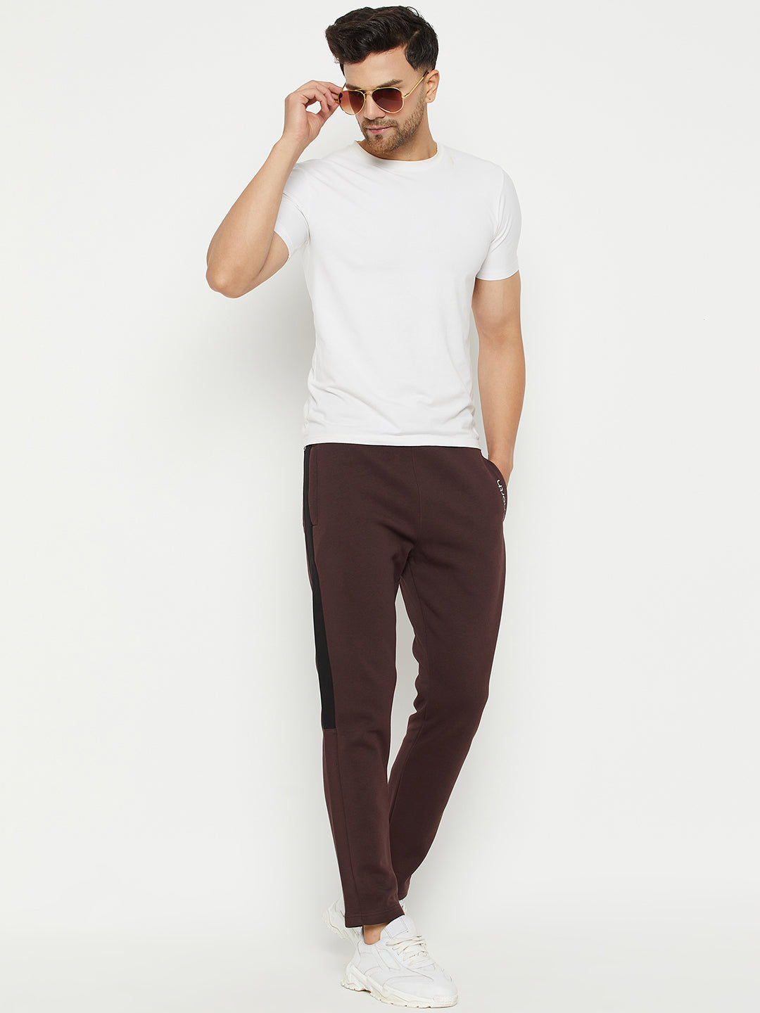 Man in sunglasses wearing a white t-shirt, maroon joggers with black side stripes, and white sneakers against a white background.