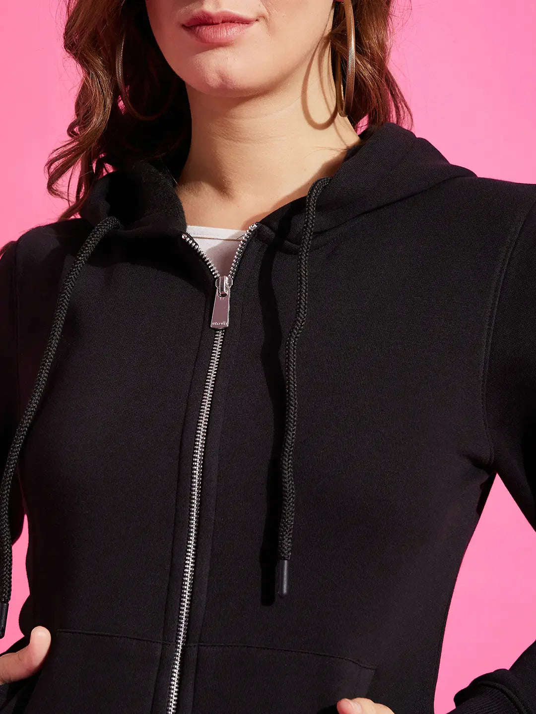 Woman wearing 98degreenorth black fleece zipper hoodie sweatshirt, posing against a bright pink background.
