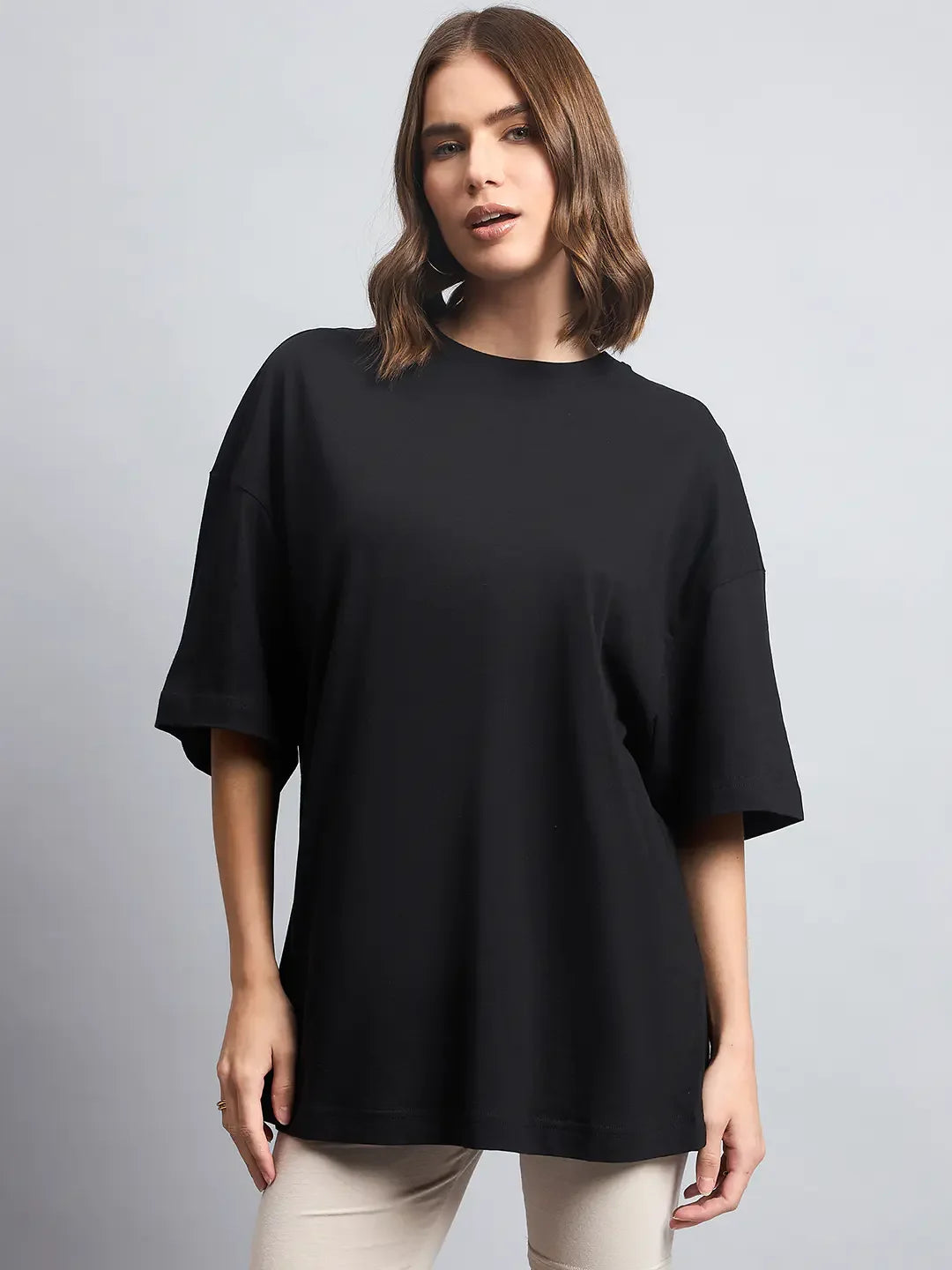 Woman with shoulder-length brown hair in a 98degreenorth Oversized Black Cotton T-Shirt, standing against a gray background.