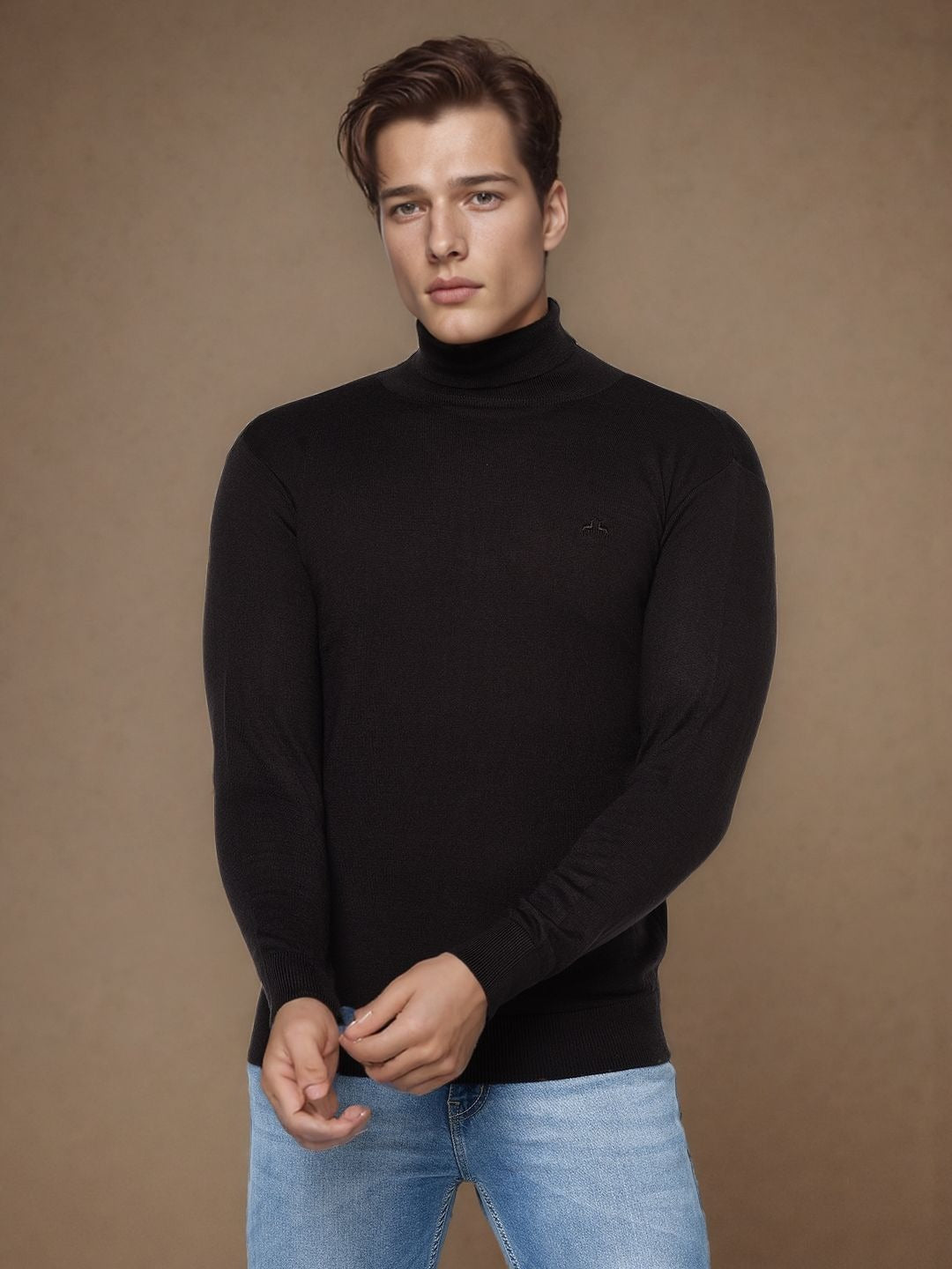 Young man in a black turtleneck sweater and blue jeans stands against a plain brown background, looking slightly serious.