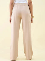 Person in Beige Wide Leg Pintuck Trackpants by 98degreenorth, white top, seen from the back against a light background.