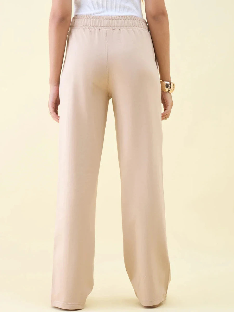 Person in Beige Wide Leg Pintuck Trackpants by 98degreenorth, white top, seen from the back against a light background.