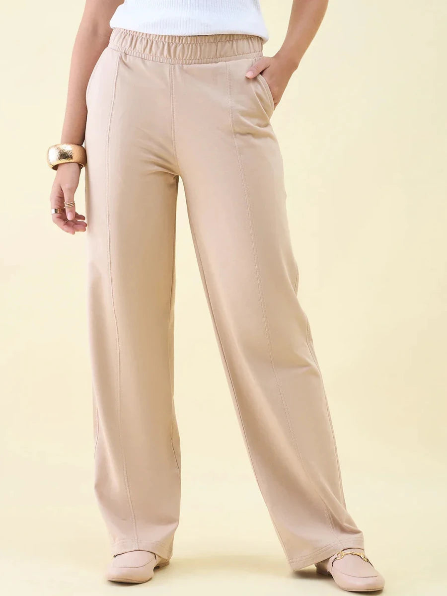 Wearing 98degreenorth Beige Wide Leg Pintuck Trackpants, white top, gold bracelets, and beige shoes, hand in pocket.