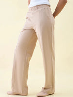 Model in Beige Wide Leg Pintuck Trackpants by 98degreenorth with a white top, sideways against a light beige backdrop.