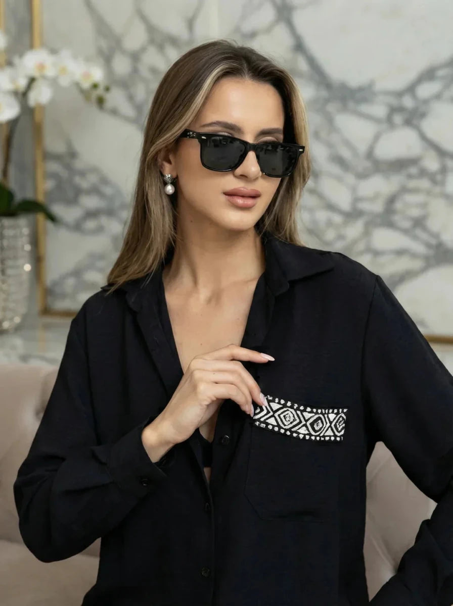 Woman in Black Aztec Embroidered Pocket Cotton Shirt by 98degreenorth, wearing black sunglasses by a marble wall.