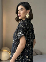 Woman with short dark hair wears the 98degreenorth Black Floral Embroidered Linen Shirt, looking over her shoulder.