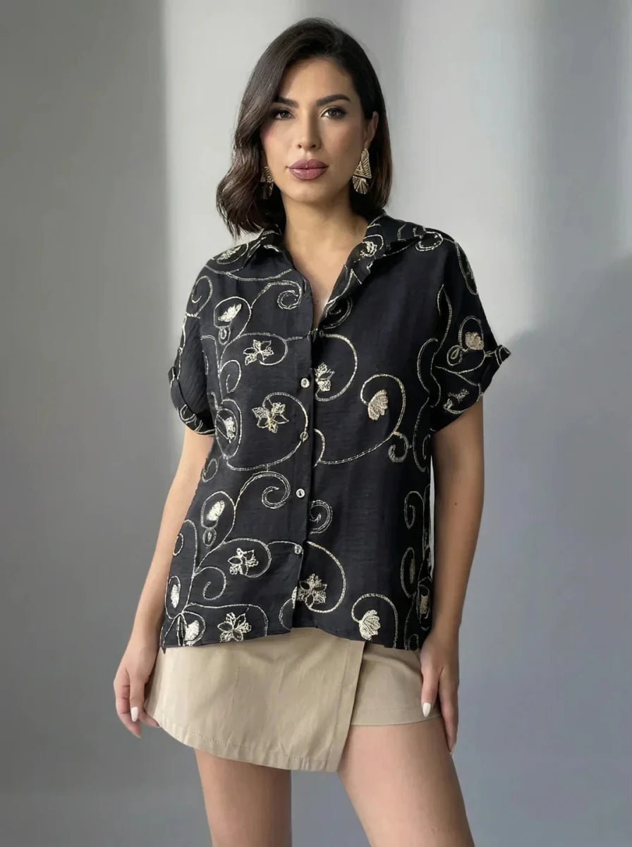 Woman wearing 98degreenorth's Black Floral Embroidered Linen Shirt with gold accents and a beige mini skirt, posing simply.