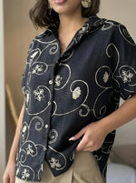 Person in 98degreenorth's Black Floral Embroidered Linen Shirt & beige pants; features luxe handcrafted botanical embroidery.