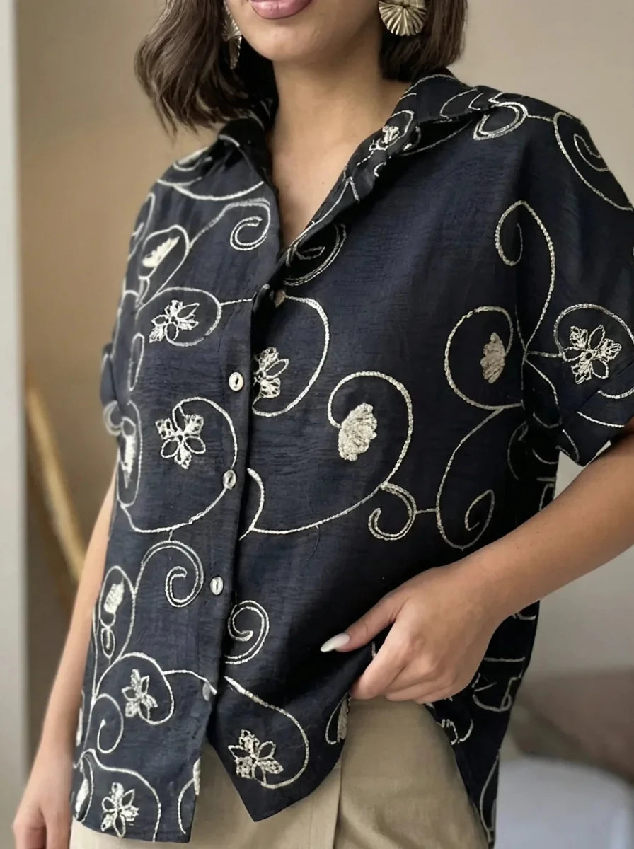 Person in 98degreenorth's Black Floral Embroidered Linen Shirt & beige pants; features luxe handcrafted botanical embroidery.