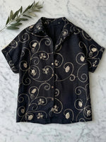 98degreenorth Black Floral Embroidered Linen Shirt—luxury summer style with gold botanical details on marble backdrop.