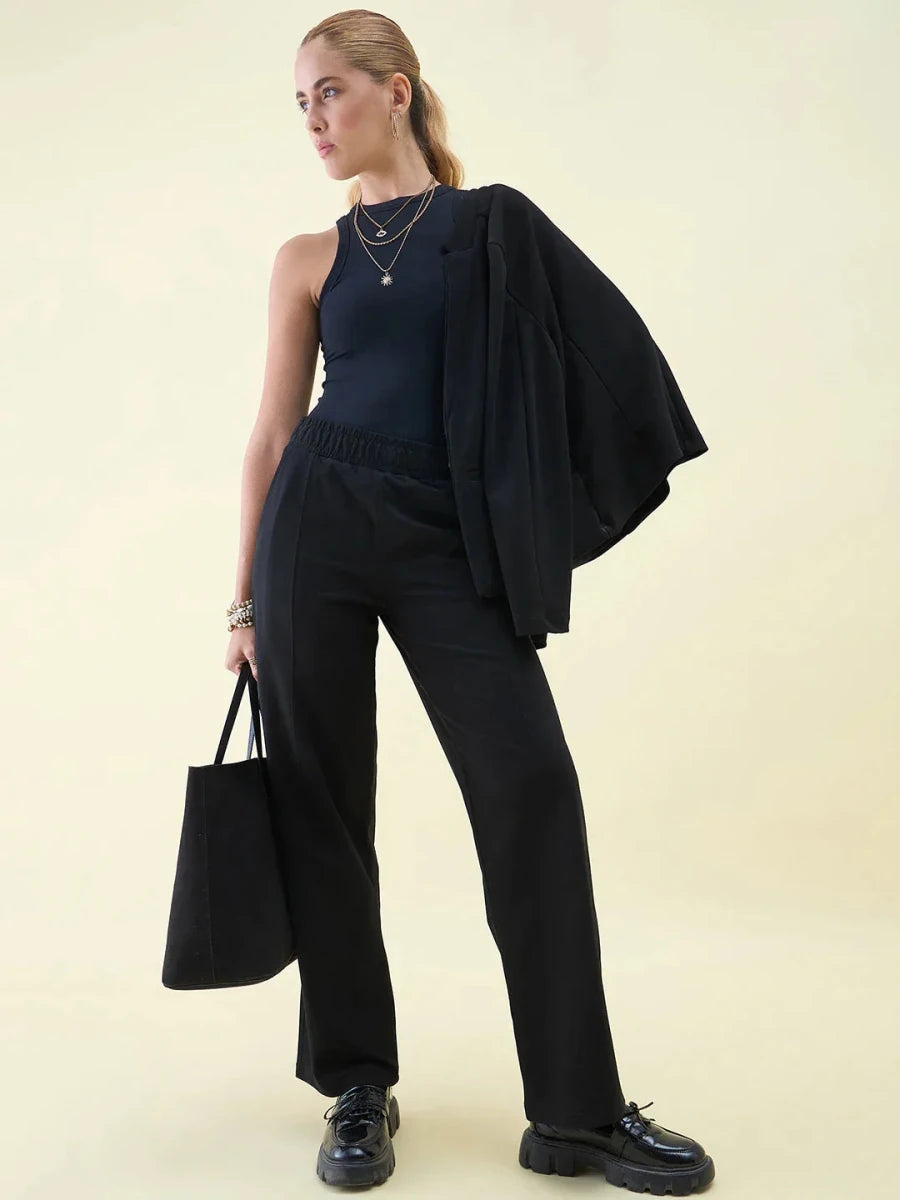 A woman in 98degreenorth Luxe Lounge Black Wide Leg Pintuck Trackpants poses confidently against a light background.