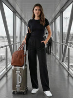 Woman wears 98degreenorth Black Wide Leg Pintuck Trackpants, standing in an airport jet bridge with luggage.