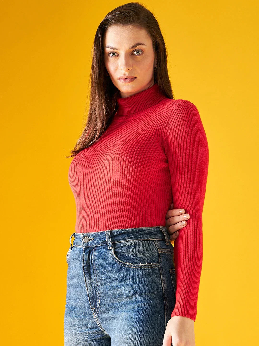 Woman in a 98degreenorth bright red ribbed turtleneck sweater, blue jeans, against a vibrant yellow background.