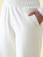 A person models 98degreenorth Butter Wide Leg Pintuck Trackpants, one hand in the pocket, showing waistband and upper leg.