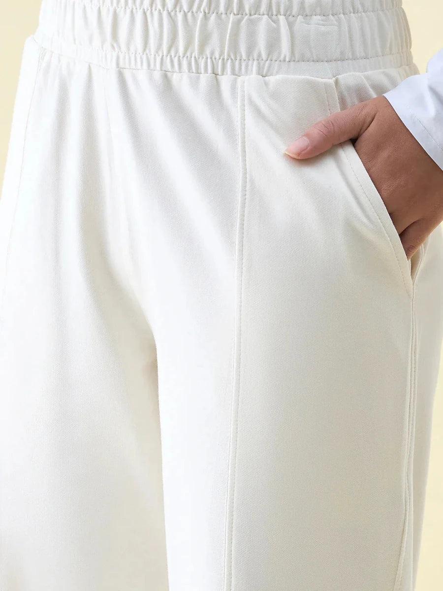A person models 98degreenorth Butter Wide Leg Pintuck Trackpants, one hand in the pocket, showing waistband and upper leg.